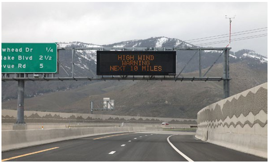 Variable message sign hung on a gantry warning drivers of high winds in a mountainous area ahead.
