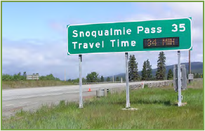 Permanent travel time advisory posted on a sign to the right of a roadway. Sign depicts distance to Snoqualmie pass and estimated travel time to reach it.
