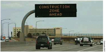 Figure 7. Existing ITS resources can be used to help manage the work zone and reduce costs. A photo shows traffic on a multilane highway with an electronic sign indicating a construction zone is ahead. Colorado DOT