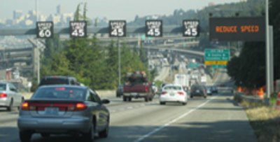 Picture of Active Traffic Management signage in Washington State showing dynamic speed limits over each lane and related warning message to reduce speed.