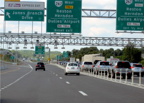Photo shows left two lanes (managed lanes) of highway with very few vehicles traveling quickly, the right two highway lanes are filed with vehicles moving slowly. Small plastic markers separate the managed lanes from other lanes.
