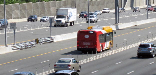 Photo of a freeway showing two directions of travel. The freeway consists of 4 general purpose and two managed lanes of travel in each direction. Plastic posts separate the different lane types. A bus, a commercial truck and passenger vehicles are traveling along the freeway.