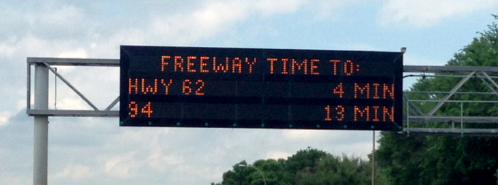 Photo of an overhead dynamic message sign indicating the freeway travel times to Highway 62 (4 minutes), and Route 94 (13 minutes).