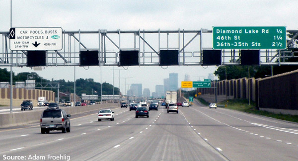Photo of I-35W in Minneapolis. The photo shows 5 lanes of one-way travel. The left lane is the managed lane, the right four lanes are general purpose lanes, an onramp and offramp are positioned on the right side of the roadway. Destination and dynamic message signage is positioned over the roadway.
