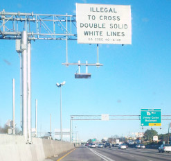 Photo of signage and electronic devices positioned above the managed lanes which indicate it is 'illegal to cross double solid white lines', and photograph and/or track toll tags.