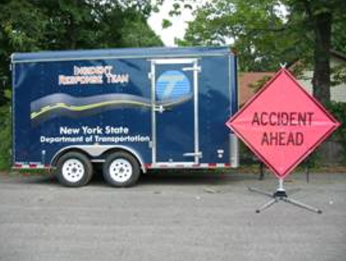 A photo of a NYSDOT Incident Response Trailer. Included in each trailer is stock to set up a temporary "Accident Protection Zone" around an incident. A temporary “Accident Ahead” sign is seen in the foreground.