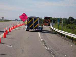 A photo of NYS Office of Fire Prevention and Control (OFPC) Incident Management Trailer parked on the side of the highway adjacent to a line of orange traffic cones blocking the use of an off-ramp. A temporary “Ramp Closed” sign can be seen in the distance.