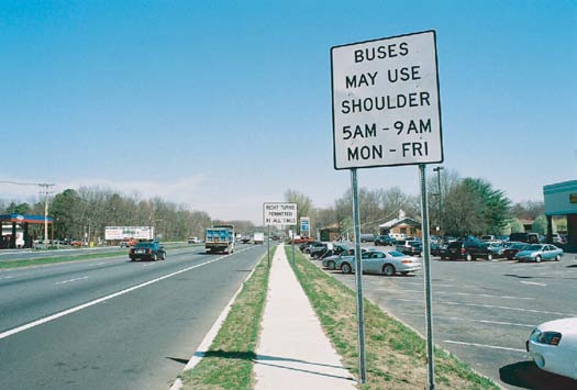 Photo of a regulatory post-mounted sign indicating “Buses may use shoulder 5AM through 9AM Monday through Friday” in black text on a white background.
