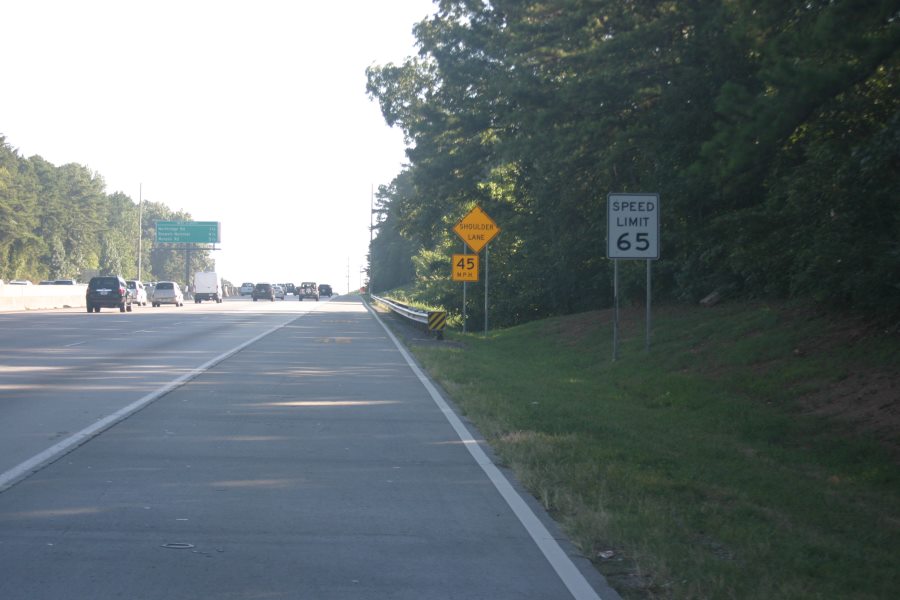 Photo of a suggested speed limit sign for the part-time shoulder lane on GA 400. The top sign is a yellow warning series sign that states, “Shoulder Lane”, the bottom rectangular warning series sign states, “45 M.P.H.” There is a typical regulatory speed limit sign upstream of the part-time shoulder sign stating the speed limit is 65 miles per hour.