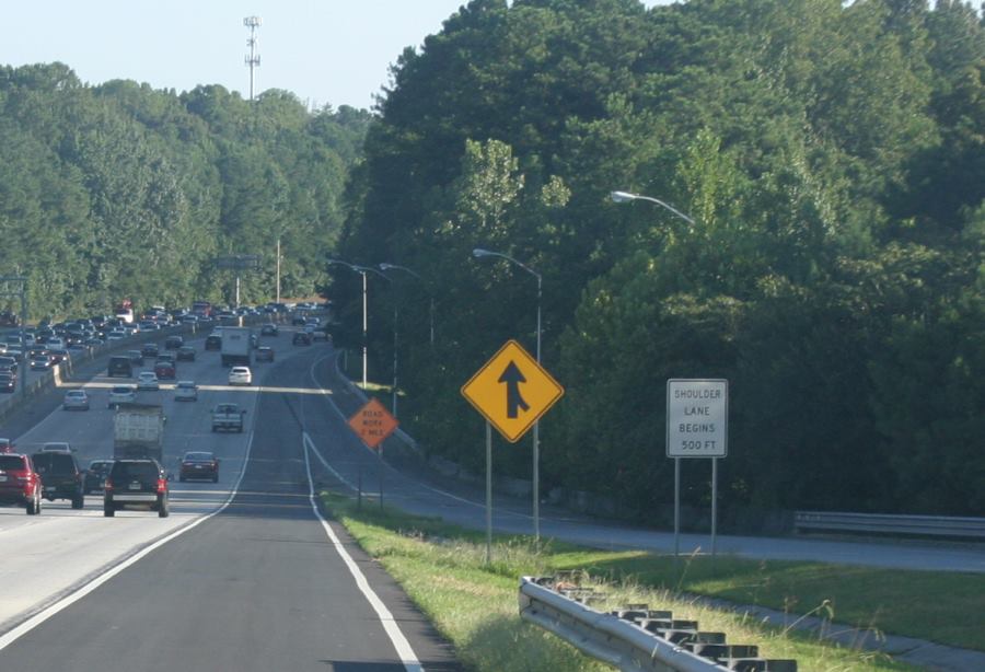Photo of a regulatory sign on the on-ramp of GA 400. The sign is place a few hundred feet upstream of the merge on the left shoulder of the on-ramp. In black text on a white background, it states, “ Shoulder lane begins 500 feet”.
