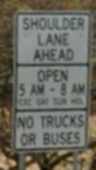 Photo of a post-mounted regulatory sign with black text on a white background. The sign states, “Shoulder lane ahead, open 5AM through 8AM Exc Sat Sun Hol, No Trucks or Buses”.
