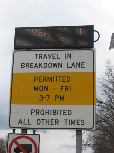 Photo of dynamic message sign added to static regulatory sign below. The dynamic sign mounted on top reads, “Breakdown lane”, while the static sign below reads, “Travel in breakdown lane, Permitted Mon through Fri 6 through 10 AM 3 through 7 PM, Prohibited all other times”.