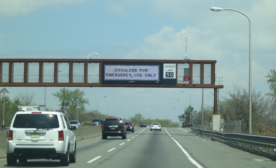 Photo of dynamic sign mounted over the travel lanes on N.J. Turnpike indicating via text the “shoulder [is] for emergency use only” and the variable speed limit, currently set at 50 m.p.h. A dynamic lane-control sign is mounted over the shoulder and is displaying a steady red ‘X’ to indicate the shoulder is currently closed.