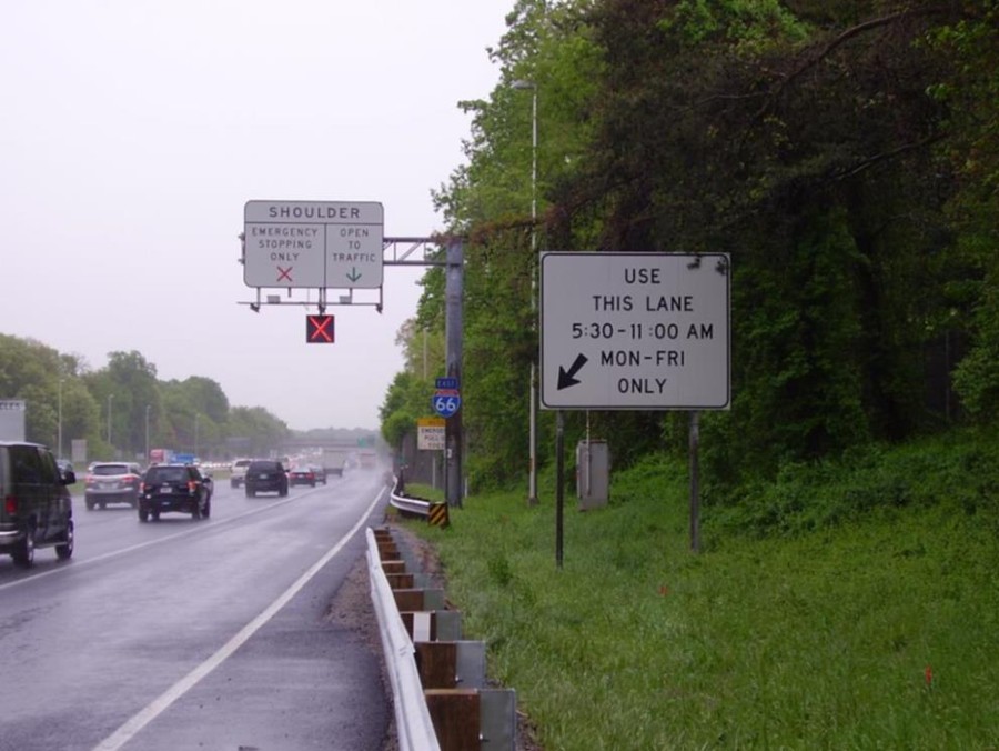 Photo of part-time shoulder operation in Northern Virginia employing multiple signs to disseminate information. These include a static roadside sign indicating the hours and days of operation, an overhead lane-use control signal displaying a steady red ‘X’ to indicate the shoulder lane is currently closed, and an overhead static sign indicating the meaning of the red ‘X’ or green arrow that can be displayed on the dynamic sign.