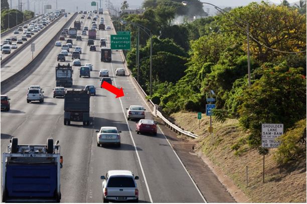 Photo showing the use of two solid, white edge lines on either side of a shoulder travel lane in Hawaii. The outside line terminates at the start of a downstream bridge. White pavement markings are used, reading “Shldr lane”.