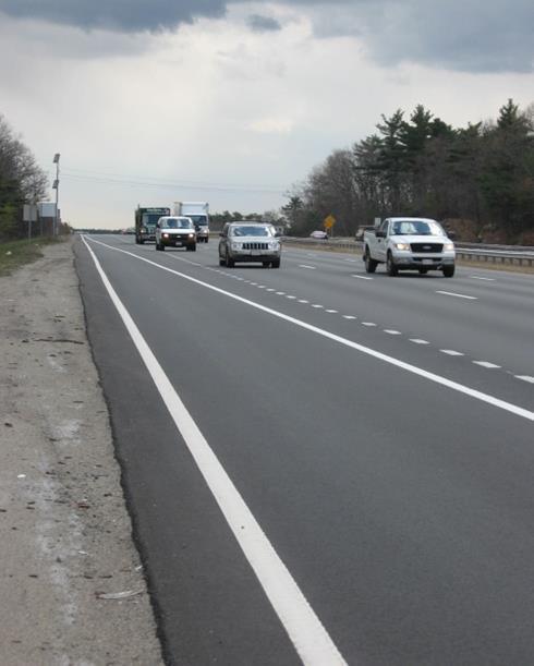 Photo of on-ramp pavement markings looking upstream at the end of an on-ramp in Massachusetts. The outside pavement marking of the shoulder lane and on-ramp lane is solid white. A solid white taper is introduced diagonally across the lane to force traffic to merge, if not using the shoulder lane. When this diagonal taper pavement marking reaches the inside edge of the lane in question, it transitions from a dotted line to a solid line.