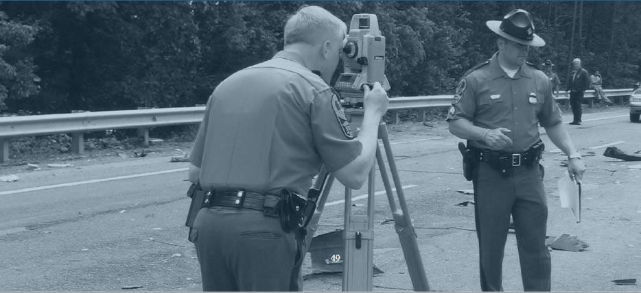 Officer using survey camera at site of car crash.