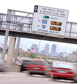 A dynamically adjusted toll rate sign on a gantry above a highway advises drivers of the cost to reach different destinations if they opt to use tolled express lanes.