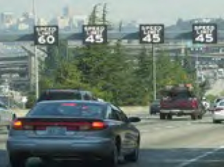 The image shows an overhead gantry with dynamic signs that display speed limit by lane.