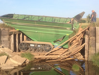 Collapsed wooden bridge with farm equipment on collapsed bridge.