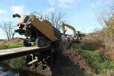 Wooden bridge with heavy mechanical equipment on it.  Yellow mechanical structure appears to be tipped up and only on two wheels.
