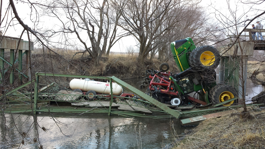 Small collapsed green wooden bridge with farm tractor overturned.
