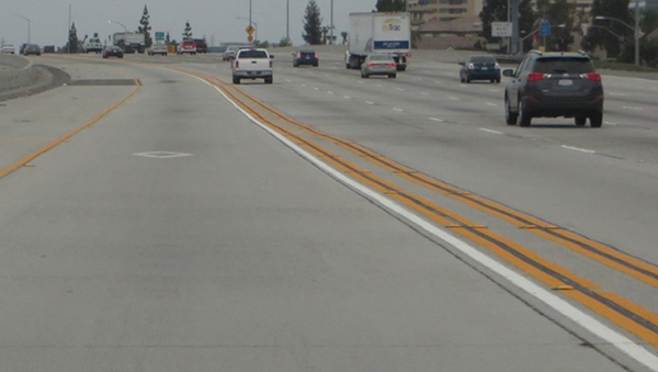 Figure 7. Graphic. Photo from a driver perspective of the buffer markings used to separate a managed lane from a general-purpose lane. The markings consist of five solid lines with a solid white line being next to the traffic in the managed lane. Beyond the solid white line are two sets of double yellow lines. The double yellow marking sets are separated by about 2 ft of pavement while within each set, the double yellow lines are separated by about 4 in of pavement.