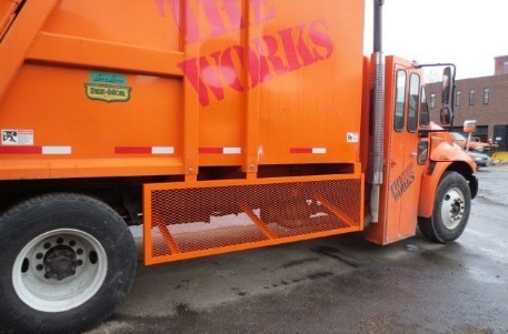 This is a picture of the side of a garbage truck with a steel mesh guard under the main body of the truck, between the passenger cabin and the rear wheel.