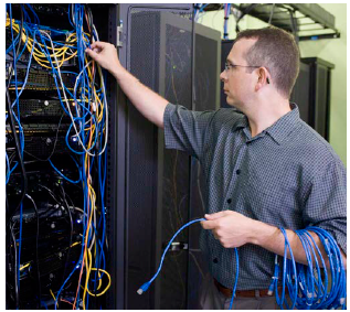 A technician running cables behind a rack of computer equipment.