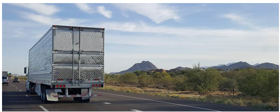 A semi traveling on a multi-lane highway in a rural area of the Southwest.