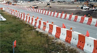 This photo shows longitudinal channelizing devices arranged to provide a barrier on both sides of a roadway—between the roadway and a construction zone on the right side and between the roadway and grass on the other.