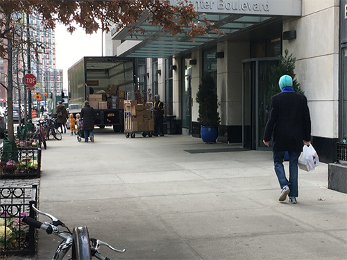 photo of a delivery person with a cart loaded with boxes at the rear of a delivery truck parked on a NYC sidewalk