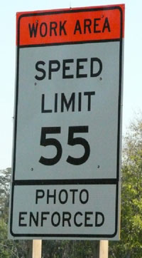 This photo shows a work zone speed limit sign which displays a speed limit of 55 miles per hour and indicates that the speed limit is photo enforced.