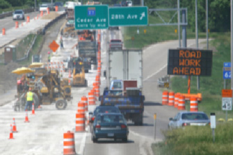 This photo shows a work zone set up in the perilous location of a highway on- and off-ramp, with a queue of cars passing very close to the work zone.