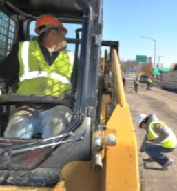 This photo shows construction workers and vehicles in a highway work zone.