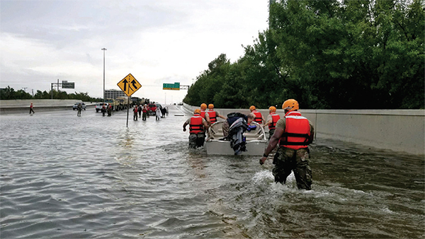 Figure 5. Photo of rescue responders wading through knee deep water on a highway while pushing a boat.