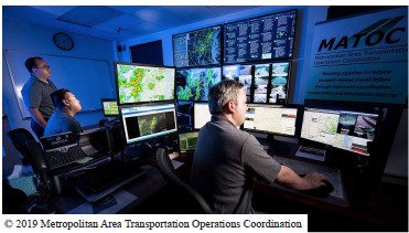 Individuals working the MATOC operations room. Monitors and panels display information such as the TweetDeck, weather maps, roadmaps, etc. Copyright 2019 Metropolitan Area Transportation Operations Coordination.