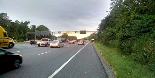 Photo shows traffic passing under a gantry with lane use signs showing speed limits and open lanes.