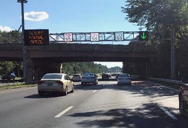 Photo shows cars on a road driving under signs that show speed limits over each lane and an arrow indicating the right shoulder is open.