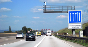 Photo shows right dynamic shoulder lane open with a car using the lane, and information on using the lane displayed in a sign on the right in German.