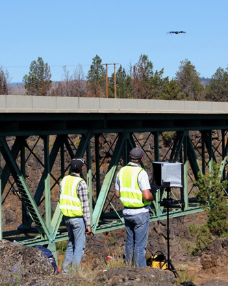 Figure 14 is a photo of two workers in reflector vests operating a drone for inspection of construction activities.