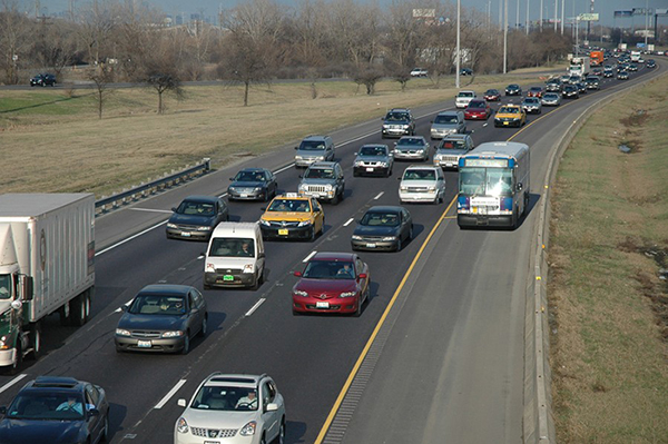 A freeway with vehicles moving into the view of the photographer.  A bus is shown on the outside of the yellow stripe, to the right and away from the other vehicles.