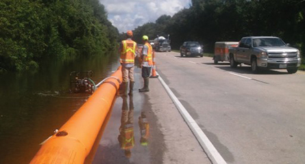 A large orange water filled tube/barrier is shown in the breakdown lane of a two-lane road...