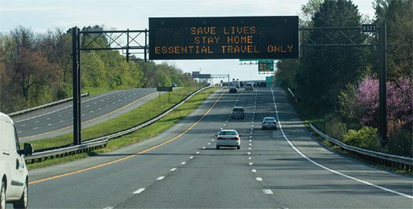 Changeable message sign above highway encouraging drivers to 'Save Lives.  Stay home.  Essential travel only.' during the COVID pandemic.