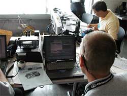 photo of two men in an office, with one man sitting at a laptop computer and another at a console