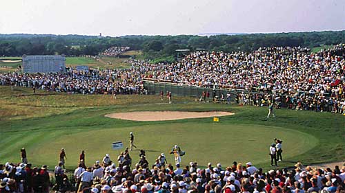 photo of a sand trap and a green at the U.S. Open golf tournament with spectators, some behind solid green barricades