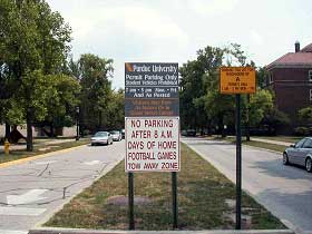 photo showing a local street sign, placed in the street median, stating "no parking after 8 a.m. days of home football games – tow away zone."