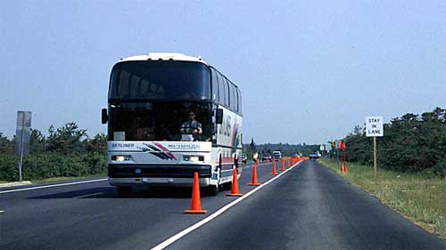 photo showing a bus traversing a center reversible lane of a two-lane arterial coned for temporary four-lane operation using the road shoulders