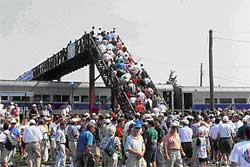 photo showing a crowd of event patrons at a commuter rail station crossing a pedestrian bridge and additional patrons waiting to cross the bridge after disembarking a train.