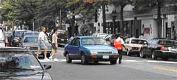 photo showing a crossing guard stopping traffic on a local street while two pedestrians traverse a mid-block crosswalk